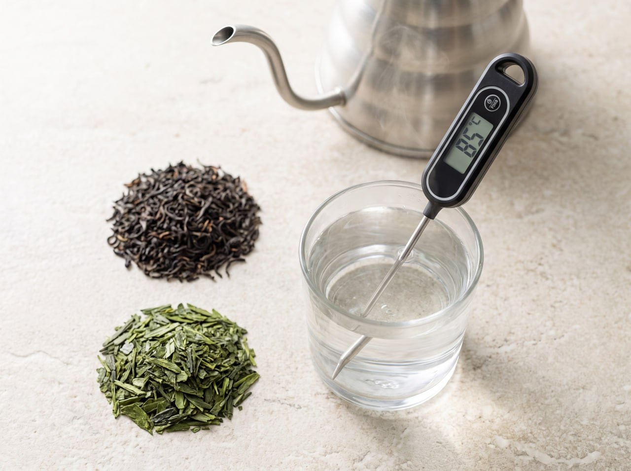 thermometer showing water temperature next to black and green tea leaves