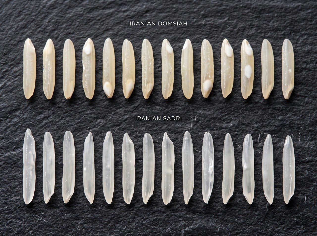 Close-up comparison of two piles of long-grain Iranian rice side by side on dark stone